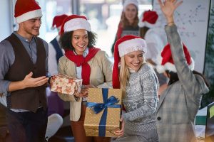 Employees celebrating the holidays with gifts and Santa hats at a workplace event