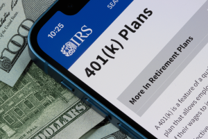 Smartphone displaying IRS 401(k) retirement plan information beside U.S. currency representing employer retirement benefits